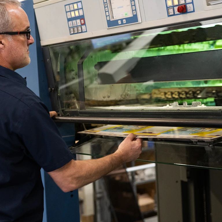 A skilled press operator at Ingersoll Paper Box meticulously oversees a high-capacity printing press in action.