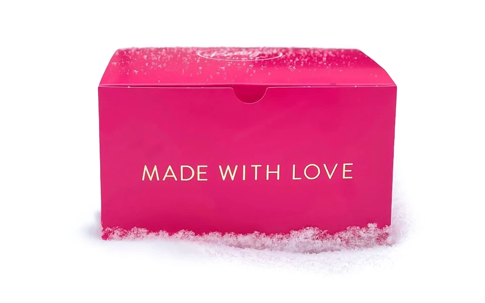Vibrant pink 'A vibrant pink box with 'MADE WITH LOVE' in bold gold lettering sits on a snowy surface, symbolizing a warm gift amidst a cold backdrop.